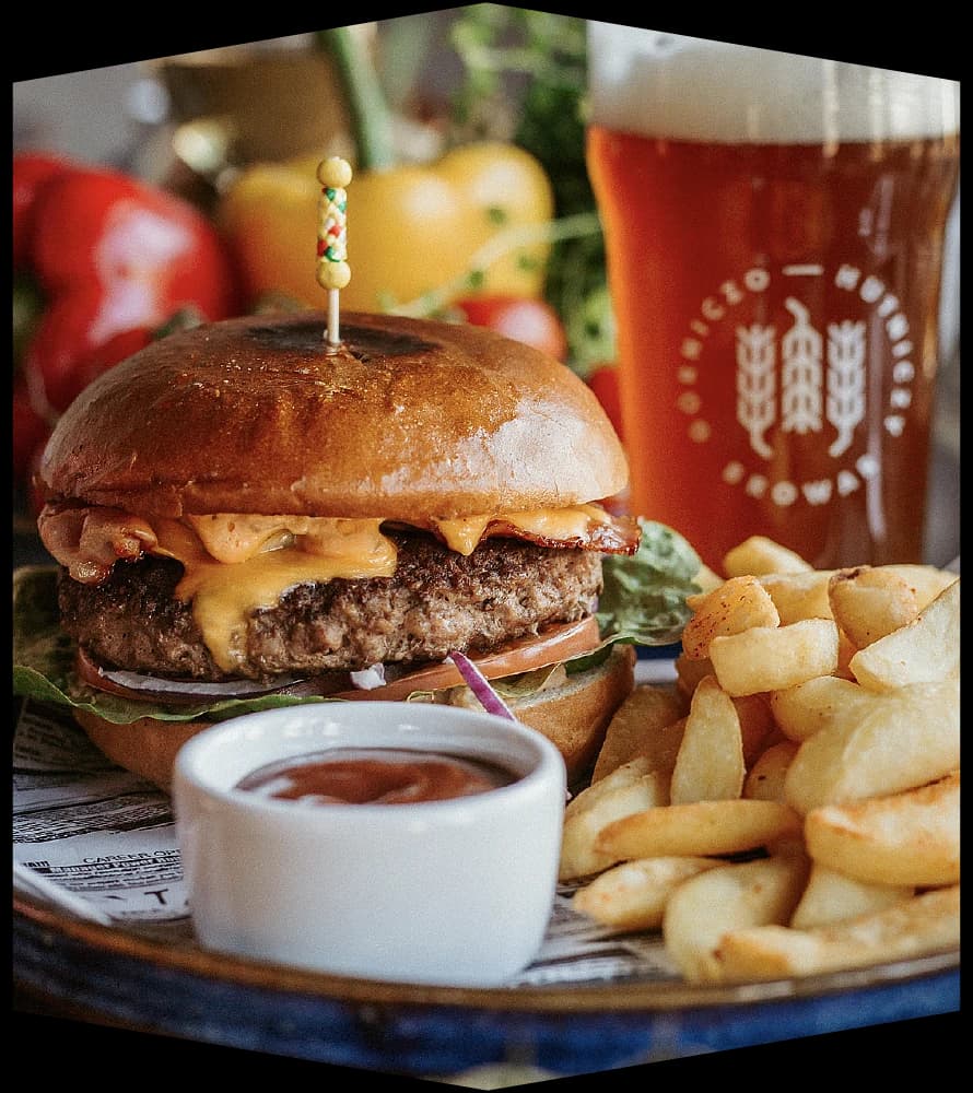 Burger z frytkami na talerzu Bistro Studio, obok szklanka piwa BGH